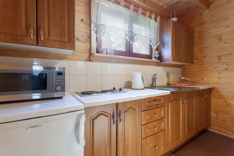Küche in einer Holzhütte mit Holzschränken, Mikrowelle, Kochplatten und Fenster in Wooden holiday cottages Pobierowo.