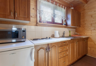 Keuken in een houten verblijf met houten kasten, microgolfoven en kookplaten in Wooden holiday cottages Pobierowo.