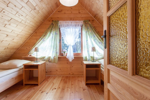 Gemütliches Schlafzimmer in einem Holzferienhaus mit Dachschräge, Fenster und zwei Einzelbetten.