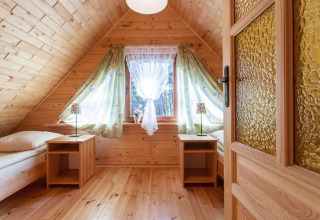 Gemütliches Schlafzimmer in einem Holzferienhaus mit Dachschräge, Fenster und zwei Einzelbetten.