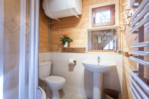 Helles Badezimmer mit Holzwänden, Waschbecken, Toilette, Fenster und Dusche in Holz-Ferienhaus.