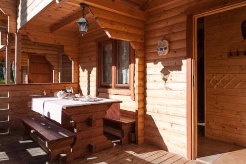 Houten terras bij Wooden holiday cottages Pobierowo met zitbank, gedekte tafel en zonlicht.