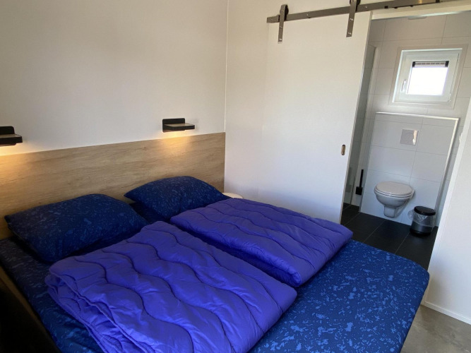 Dormitorio con cama doble, ropa de cama morada y baño en suite en Zonneweelde Lodge Deluxe, Países Bajos.