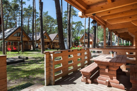 Holzferienhäuser Pobierowo in einem sonnigen Waldgebiet mit Veranda und Picknicktisch im Vordergrund.