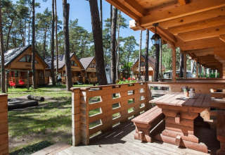 Houten vakantiehuisjes Pobierowo in een bosrijke omgeving met zon, veranda en picknicktafel vooraan.