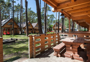 Træferiehytter Pobierowo i skovområde med solskin, træterrasse og picnicbord i forgrunden.