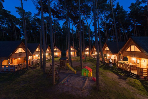 Verlichte houten vakantiehuisjes 's nachts met speeltuin en zandbak, Wooden holiday cottages Pobierowo in Duitsland.