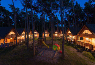 Verlichte houten vakantiehuisjes 's nachts met speeltuin en zandbak, Wooden holiday cottages Pobierowo in Duitsland.