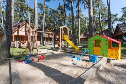 Speelplein met zandbak, glijbaan en speelhuis nabij houten vakantiehuisjes in het bos van Pobierowo.