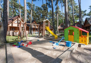 Speelplaats met zandbak, glijbaan en speelhuisje voor houten vakantiehuisjes in het bos van Pobierowo.