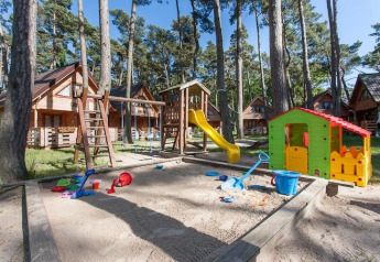 Parco giochi con sabbiera, scivolo e casetta davanti a chalet in legno immersi nei boschi di Pobierowo.