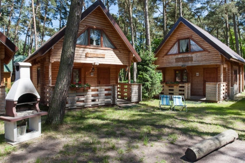 Holzferienhäuser in einem grünen Waldgebiet mit Grillplatz und Gartenstühlen in Pobierowo, Deutschland.