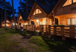 Abendaufnahme von beleuchteten Holzhütten mit Veranda bei «Wooden holiday cottages Pobierowo» in Deutschland.