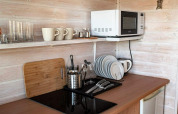 Pequeña cocina con microondas, tazas, vasos y platos en una cabaña de madera en Alemania.