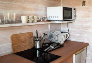 Small kitchenette with microwave, cups, glasses and plates in a wooden cabin in Germany.