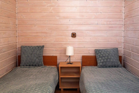 Twee eenpersoonsbedden met groene dekens en kussens, houten muren en nachtkastje in Aquarius Cottages, Duitsland.