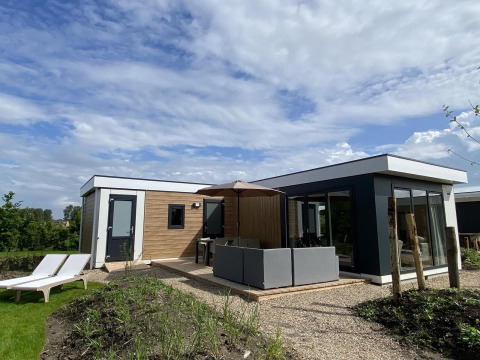 Lodge Zonneweelde XL moderno en Camping Zonneweelde, Países Bajos, con terraza, sofá y tumbonas en el jardín.