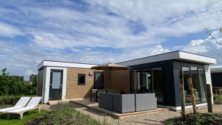 Lodge Zonneweelde XL moderno en Camping Zonneweelde, Países Bajos, con terraza, sofá y tumbonas en el jardín.