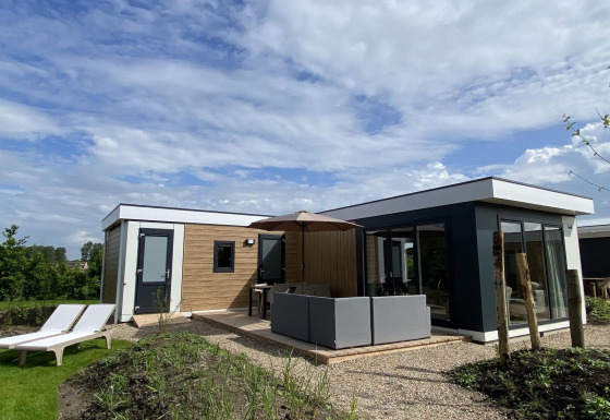 Lodge Zonneweelde XL moderno en Camping Zonneweelde, Países Bajos, con terraza, sofá y tumbonas en el jardín.