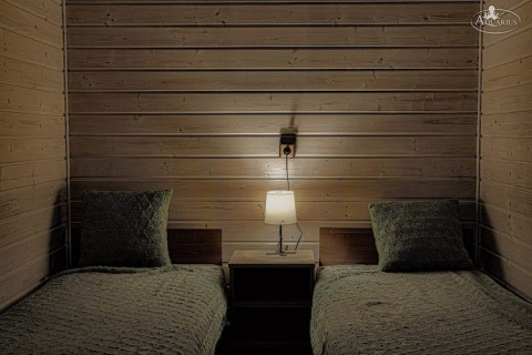 To enkeltsenge med grønne tæpper og hovedpuder i Aquarius Cottages, tyskl træindretning og natlampe.