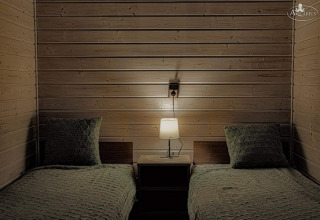 Two single beds with green bedding and pillows, lamp on a nightstand in a wooden Aquarius Cottages cabin.