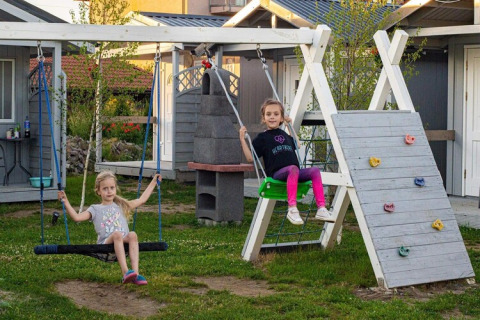 Zwei Kinder schaukeln und spielen an einer Kletterwand vor einem Ferienhaus bei Aquarius Cottages, Deutschland.