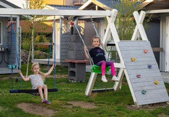 Twee kinderen spelen op schommels en een klimmuur voor een huisje bij Aquarius Cottages in Duitsland.