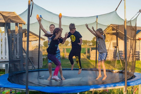 Vier kinderen springen samen op een trampoline naast een chalet van Aquarius Cottages in Duitsland.