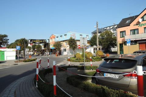 Street view near Aquarius Cottages with parked cars, shops, and a campground in the background, Germany