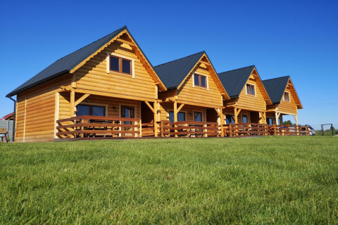 Cuatro cabañas de madera con porches en un campo verde bajo un cielo azul en Lazurowy Zakątek lodge.
