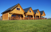 Vier Holzchalets mit Veranda auf einer grünen Wiese unter blauem Himmel bei der Lazurowy Zakątek-Lodge.