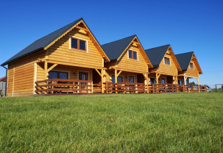 Cuatro cabañas de madera con porches en un campo verde bajo un cielo azul en Lazurowy Zakątek lodge.