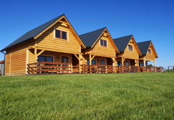 Quattro chalet in legno con veranda su un prato verde sotto un cielo blu presso il lodge Lazurowy Zakątek.