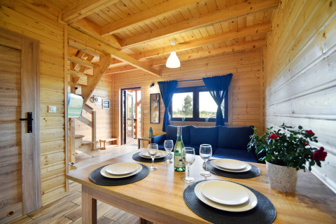 Interior de madera clara en Lazurowy Zakątek, Alemania, con mesa puesta y cortinas azules.