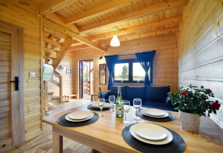 Licht houten interior in Lazurowy Zakątek lodge te Duitsland met gedekte tafel en blauwe gordijnen.