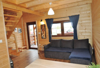 Sala en la cabaña «Lazurowy Zakątek» en Alemania con sofá azul, paredes de madera y gran ventana.
