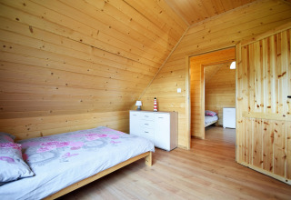 Slaapkamer met houten lambrisering, enkel bed en witte kast bij Lazurowy Zakątek lodge in Duitsland.