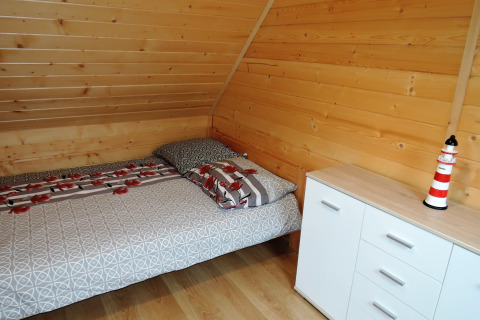 Dormitorio acogedor con paredes de madera, cama doble, cómoda blanca y figura de faro decorativa.