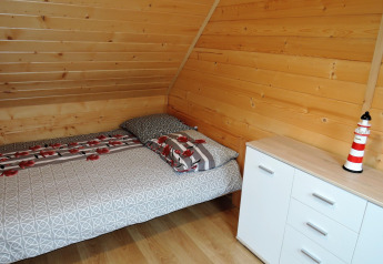 Camera accogliente con pareti in legno, letto matrimoniale, cassettiera bianca e decorazione a faro.