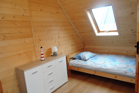 Habitación con paneles de madera en Lazurowy Zakątek, cama individual, cómoda y ventana en el techo.