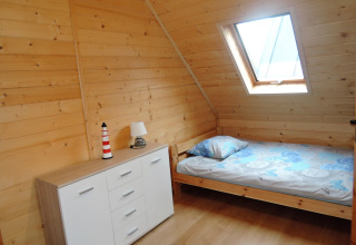 Habitación con paneles de madera en Lazurowy Zakątek, cama individual, cómoda y ventana en el techo.