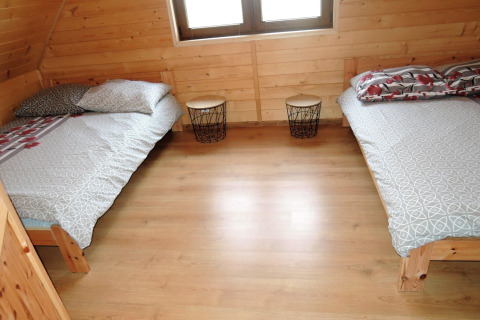 Twee eenpersoonsbedden in een houten kamer van Lazurowy Zakątek-lodge, met nachtkastjes ertussen.