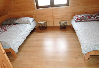Dos camas individuales en una habitación de madera en la posada Lazurowy Zakątek, con mesitas entre ellas.