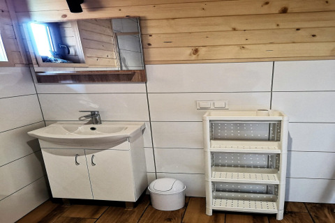 Moderne badkamer met witte wastafel, spiegelkast, vuilbakje en wit rek tegen houten en betegelde muren.