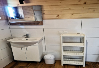 Baño moderno con lavabo blanco, espejo, papelera y estantería blanca sobre paredes de madera y azulejos.