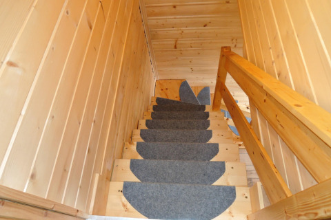 Houten trap met grijze tapijtlopers in Lazurowy Zakątek lodge, Duitsland, opwaartse kijk met leuning.