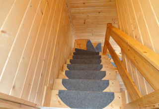 Houten trap met grijze tapijtlopers in Lazurowy Zakątek lodge, Duitsland, opwaartse kijk met leuning.