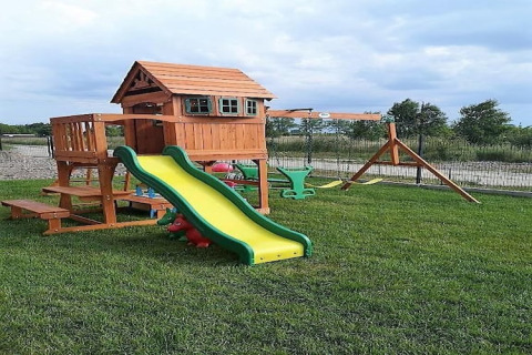 Parque infantil exterior con casita de madera, tobogán y columpios en la posada Lazurowy Zakątek en Alemania.