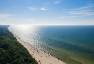 Vista aérea desde Lazurowy Zakątek: playa de arena, mar azul y costa boscosa bajo un cielo soleado.