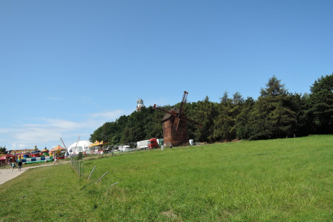 Campo verde con un molino de viento, árboles y una colorida zona de parque de atracciones al fondo.